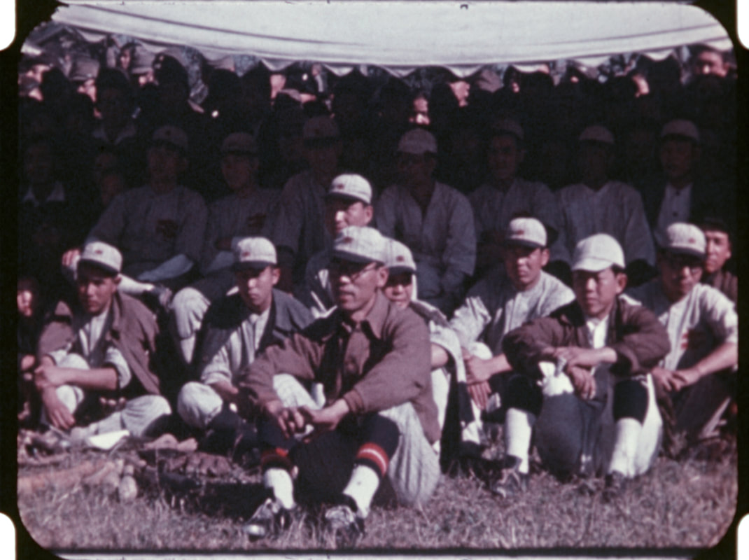 Japanese baseball players in uniforms sitting in the grass.